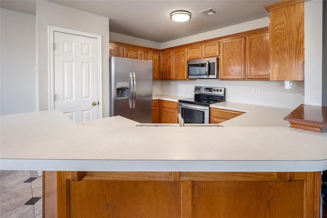 1704 Sumac Dr, Norman, OK 73071 - kitchen with appliances with stainless steel finishes, light countertops, a peninsula, and brown cabinetry