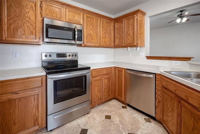 1704 Sumac Dr, Norman, OK 73071 - kitchen featuring appliances with stainless steel finishes, light countertops, ceiling fan, and brown cabinetry