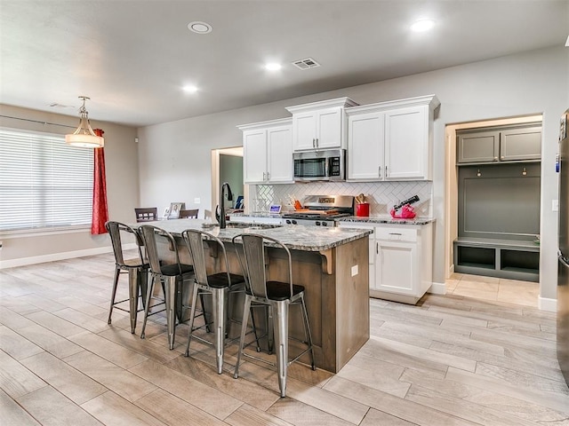 1405 Atalon Dr, Moore, OK 73160 - kitchen with appliances with stainless steel finishes, a kitchen bar, decorative backsplash, wood finish floors, and recessed lighting