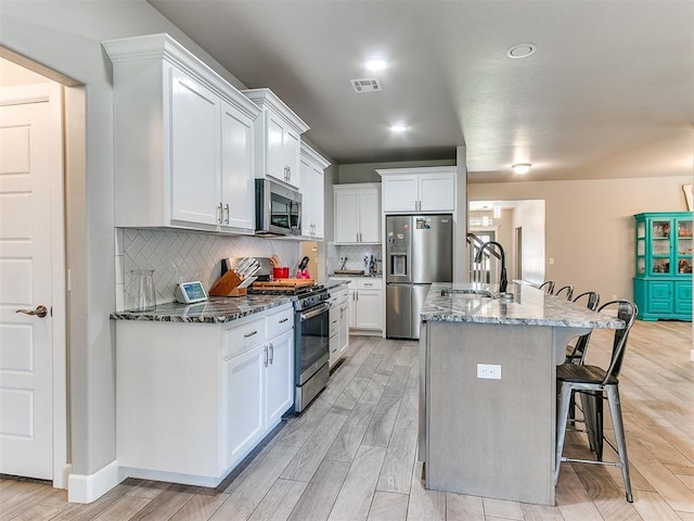 1405 Atalon Dr, Moore, OK 73160 - kitchen with appliances with stainless steel finishes, a sink, a kitchen breakfast bar, dark stone counters, and light wood-style floors