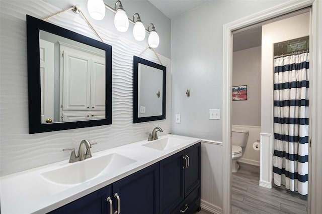 1704 Faircloud Dr, Edmond, OK 73034 - full bathroom featuring double vanity, toilet, wood finished floors, and a wainscoted wall