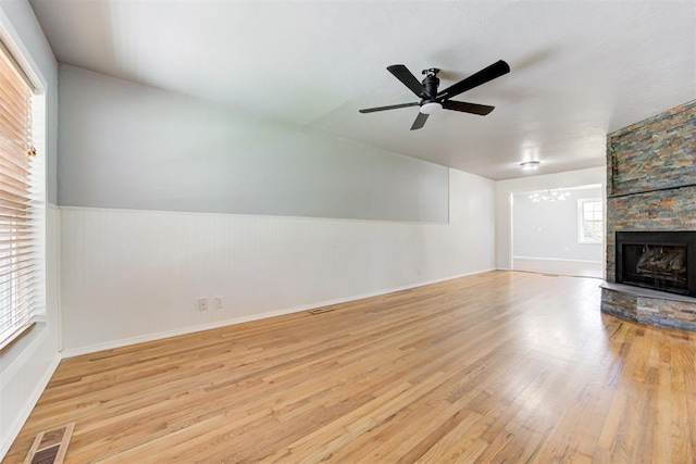 1206 Monroe Dr, Shawnee, OK 74804 - unfurnished living room with wood finished floors, a chandelier, ceiling fan, a stone fireplace, and wainscoting