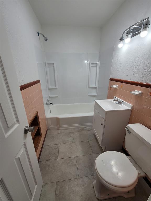 1228 Santa Fe Dr, Clinton, OK 73601 - bathroom with tile walls, toilet, shower / bathtub combination, vanity, and a wainscoted wall