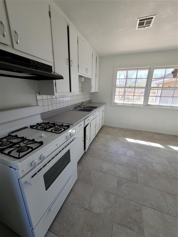 1228 Santa Fe Dr, Clinton, OK 73601 - kitchen featuring white gas stove, under cabinet range hood, backsplash, white cabinets, and a sink