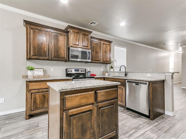 8344 NW 137th St, Oklahoma City, OK 73142 - kitchen with stainless steel appliances, a sink, a peninsula, light wood-type flooring, and ornamental molding