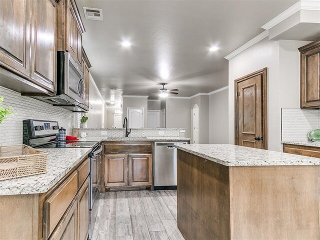 8344 NW 137th St, Oklahoma City, OK 73142 - kitchen featuring appliances with stainless steel finishes, a sink, tasteful backsplash, a peninsula, and light wood finished floors