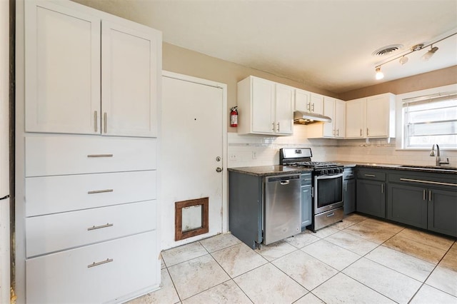 3901 NW 56th Pl, Oklahoma City, OK 73112 - kitchen featuring appliances with stainless steel finishes, a sink, under cabinet range hood, backsplash, and white cabinetry