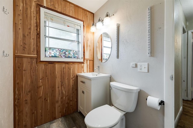 3901 NW 56th Pl, Oklahoma City, OK 73112 - half bathroom with wood finished floors, wooden walls, vanity, toilet, and healthy amount of natural light