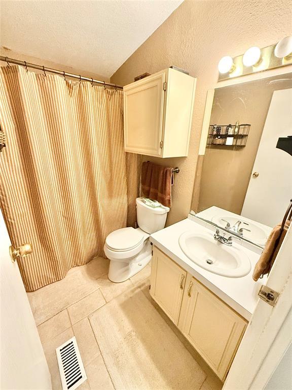 305 N Greer Ave, Duke, OK 73532 - full bathroom with a textured ceiling, toilet, vanity, tile patterned floors, and lofted ceiling