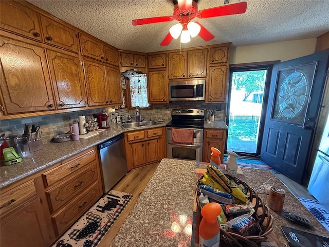 kitchen with appliances with stainless steel finishes, brown cabinetry, a sink, a textured ceiling, and a ceiling fan