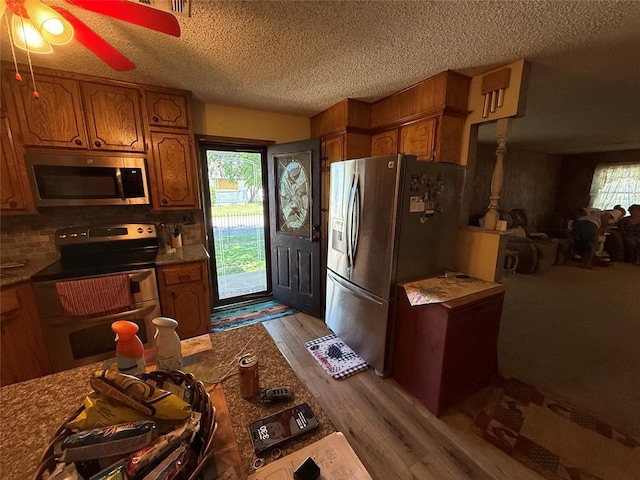 kitchen with stainless steel appliances, brown cabinetry, a textured ceiling, wood finished floors, and tasteful backsplash