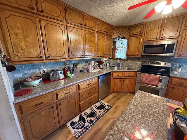 kitchen with appliances with stainless steel finishes, a sink, brown cabinets, light wood-type flooring, and decorative backsplash