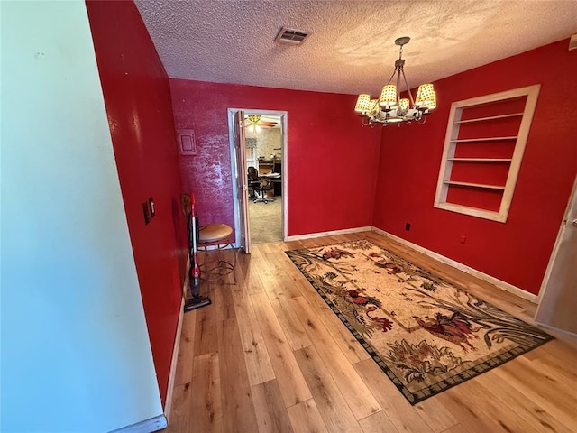 dining area with a textured ceiling, a chandelier, wood-type flooring, built in shelves, and baseboards