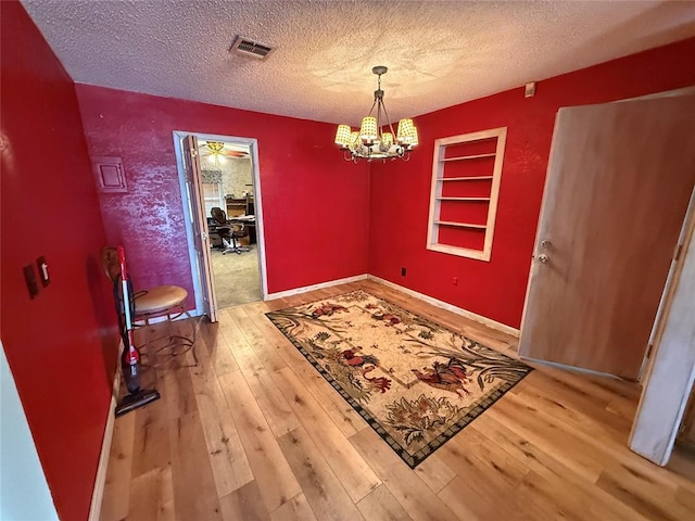 dining space with a textured ceiling, a chandelier, hardwood / wood-style flooring, and built in features