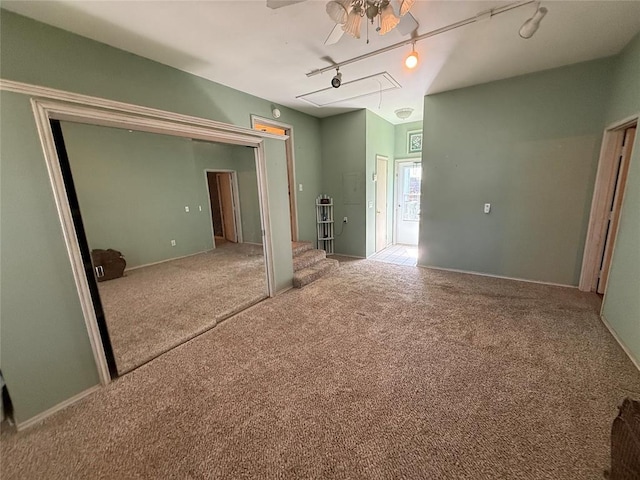 unfurnished bedroom featuring attic access, rail lighting, carpet, and ceiling fan