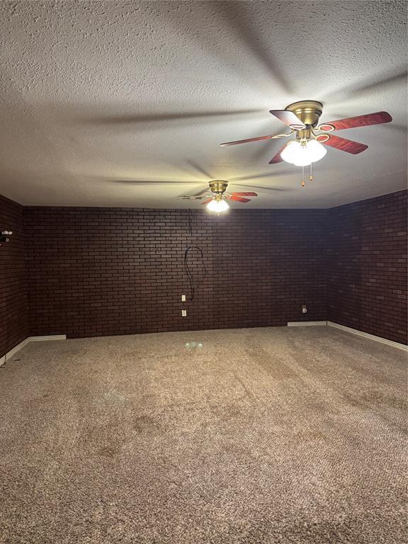 spare room featuring brick wall, carpet flooring, a textured ceiling, a ceiling fan, and baseboards