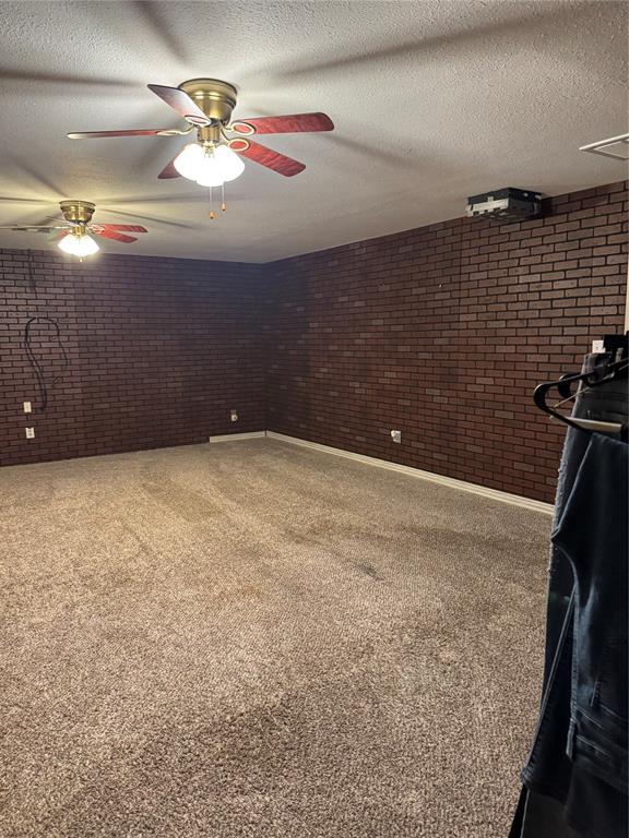 carpeted spare room with brick wall, a ceiling fan, a textured ceiling, and baseboards
