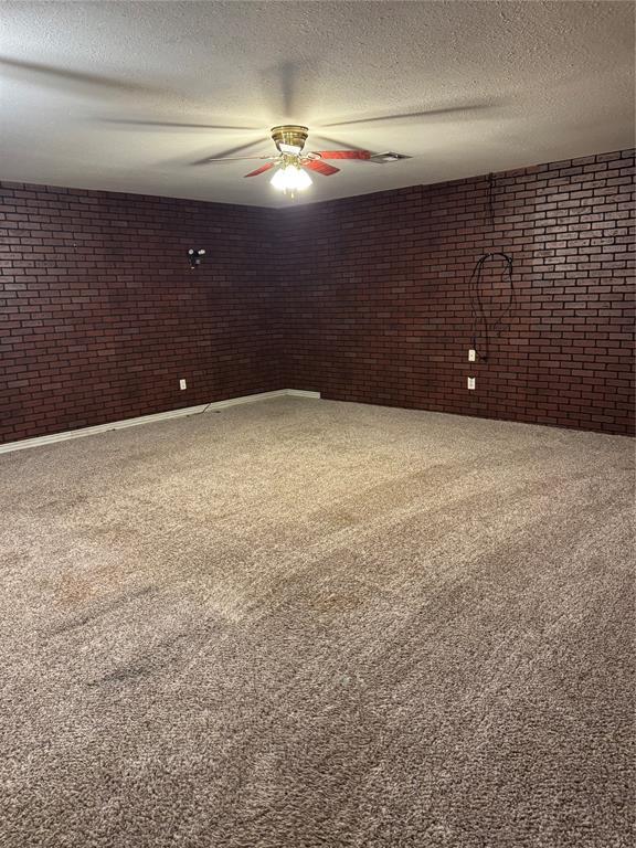 unfurnished room with carpet flooring, brick wall, a textured ceiling, baseboards, and ceiling fan