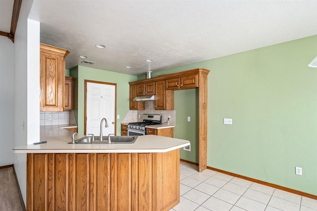 11014 Madison Ave, Midwest City, OK 73130 - kitchen featuring stainless steel gas range, under cabinet range hood, a sink, decorative backsplash, and a peninsula