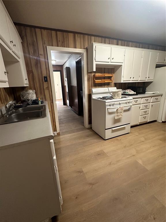 408 Wake St, Broken Bow, OK 74728 - kitchen featuring white appliances, a sink, light wood finished floors, white cabinets, and wooden walls