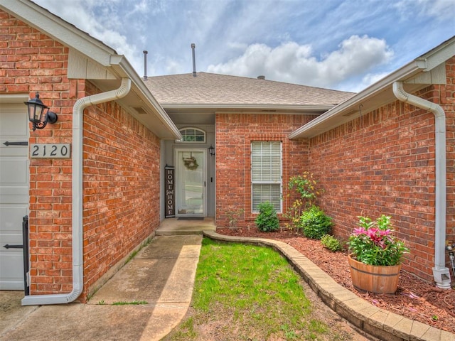 2120 NE 4th St, Moore, OK 73160 - doorway to property featuring brick siding, a shingled roof, and an attached garage