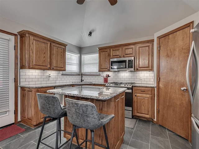 2120 NE 4th St, Moore, OK 73160 - kitchen featuring stainless steel appliances, a sink, vaulted ceiling, brown cabinets, and a kitchen bar