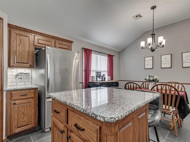 2120 NE 4th St, Moore, OK 73160 - kitchen with freestanding refrigerator, dark tile patterned floors, brown cabinetry, a kitchen island, and vaulted ceiling