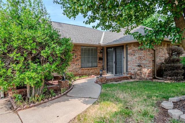 5821 NW 89th St, Oklahoma City, OK 73132 - doorway to property with brick siding, a shingled roof, and a lawn