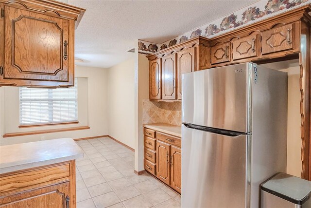 5821 NW 89th St, Oklahoma City, OK 73132 - kitchen featuring freestanding refrigerator, light countertops, tasteful backsplash, brown cabinets, and light tile patterned floors