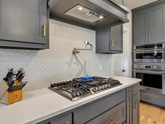 4315 Dusty Trl, Norman, OK 73072 - kitchen with stainless steel appliances, gray cabinetry, light countertops, decorative backsplash, and light wood finished floors