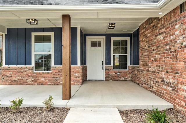 10412 SW 49th St, Mustang, OK 73064 - view of exterior entry with board and batten siding, roof with shingles, brick siding, and covered porch