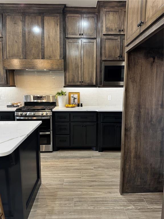 10421 SW 50th St, Mustang, OK 73064 - kitchen featuring stainless steel gas range, wood finish floors, ventilation hood, backsplash, and dark brown cabinets