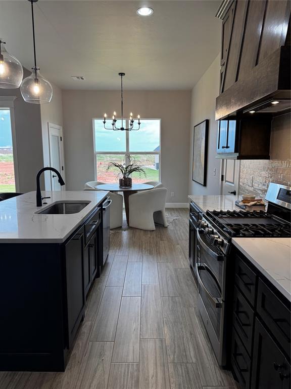 10421 SW 50th St, Mustang, OK 73064 - kitchen with stainless steel appliances, ventilation hood, a chandelier, tasteful backsplash, and light wood-style flooring