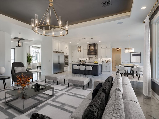 1117 Falls Bridge Ct, Edmond, OK 73034 - living room with a chandelier, recessed lighting, light marble finish floors, baseboards, and a tray ceiling