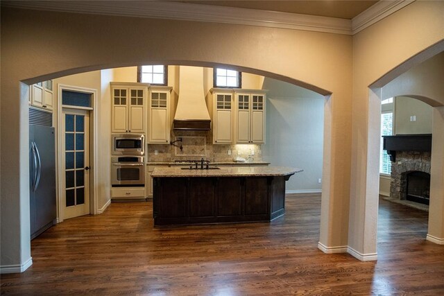 3176 E 146th Pl, Bixby, OK 74008 - kitchen with custom range hood, built in appliances, a center island with sink, crown molding, and light stone countertops