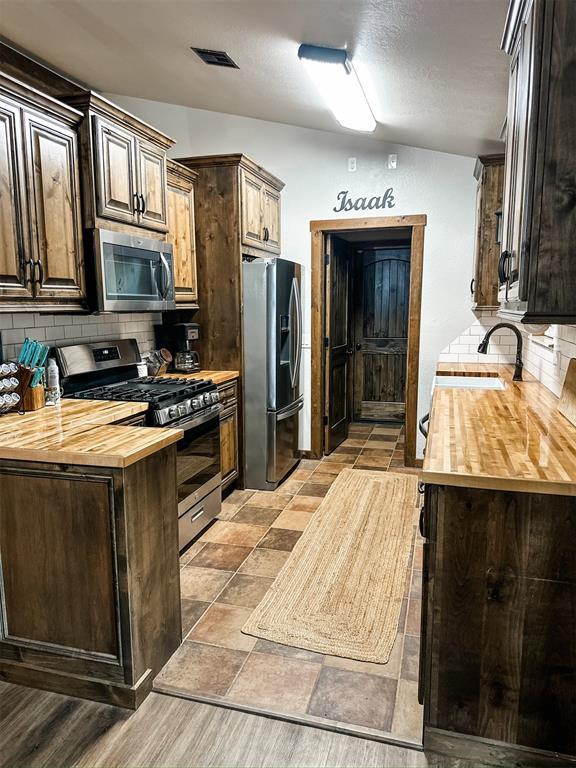 1913 Linwood St, Weatherford, OK 73096 - kitchen featuring wood counters, stainless steel appliances, backsplash, dark brown cabinets, and vaulted ceiling