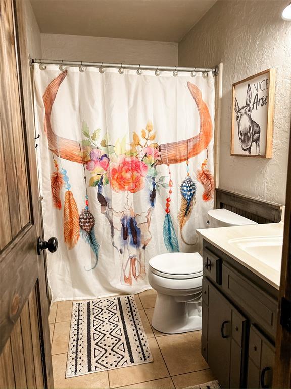 1913 Linwood St, Weatherford, OK 73096 - bathroom featuring a textured wall, vanity, toilet, tile patterned floors, and curtained shower
