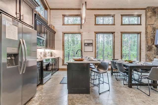 166 Morning Berry Trl, Broken Bow, OK 74728 - kitchen with stainless steel appliances, wood walls, concrete flooring, an island with sink, and a kitchen breakfast bar