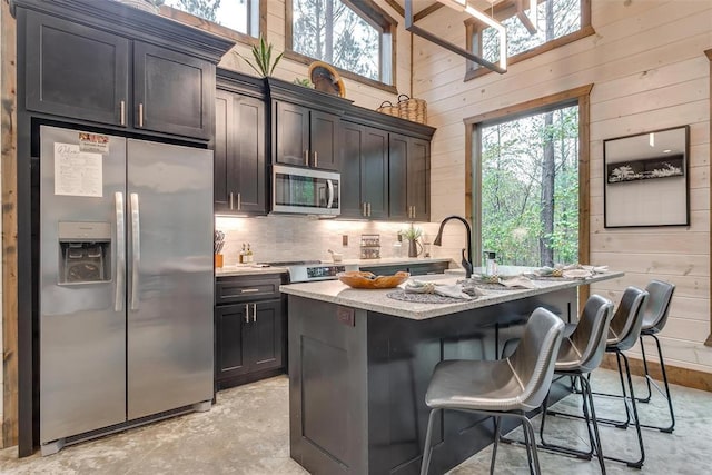 166 Morning Berry Trl, Broken Bow, OK 74728 - kitchen featuring stainless steel appliances, healthy amount of natural light, wooden walls, a breakfast bar area, and light stone countertops