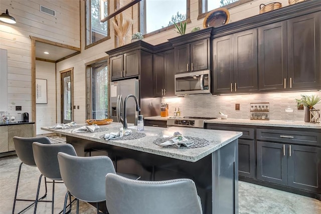 166 Morning Berry Trl, Broken Bow, OK 74728 - kitchen featuring stainless steel appliances, wooden walls, a towering ceiling, a breakfast bar, and decorative backsplash
