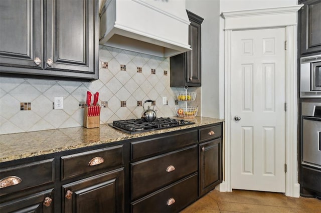 4605 NW 161st St, Edmond, OK 73013 - kitchen with premium range hood, stainless steel appliances, tasteful backsplash, light stone countertops, and dark brown cabinets