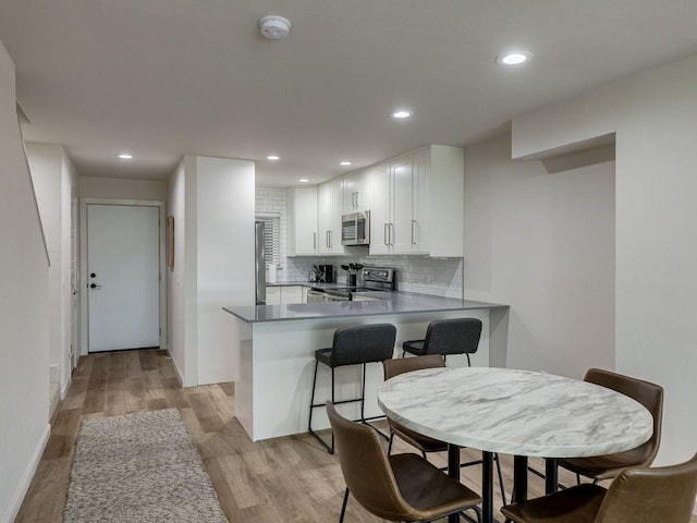 1110 Sherwood Ln Unit 223, Nichols Hills, OK 73116 - kitchen with appliances with stainless steel finishes, light wood-style floors, a peninsula, tasteful backsplash, and white cabinetry