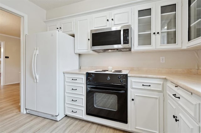 3119 W Wilshire Blvd, Oklahoma City, OK 73116 - kitchen with stainless steel microwave, electric range, freestanding refrigerator, light wood finished floors, and white cabinets