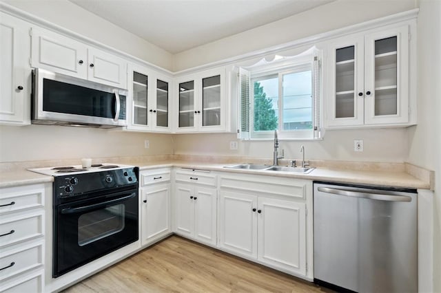 3119 W Wilshire Blvd, Oklahoma City, OK 73116 - kitchen featuring appliances with stainless steel finishes, a sink, white cabinets, light wood-style floors, and glass insert cabinets