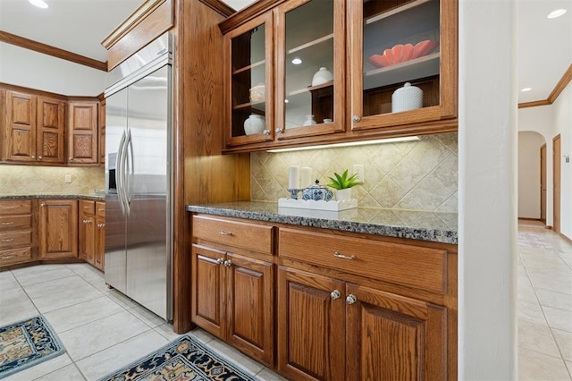 607 Pool Pl, Shawnee, OK 74801 - kitchen featuring stainless steel built in refrigerator, crown molding, brown cabinetry, light tile patterned flooring, and dark stone countertops