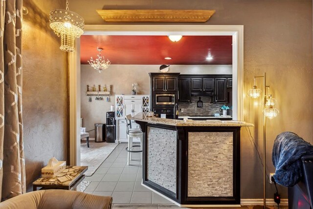 704 N Geronimo Way, Mustang, OK 73064 - kitchen with a chandelier, tasteful backsplash, light tile patterned flooring, stainless steel microwave, and light stone countertops