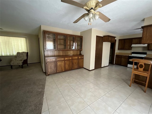 3014 S Mission St, Anadarko, OK 73005 - kitchen featuring electric stove, under cabinet range hood, a ceiling fan, glass insert cabinets, and light tile patterned flooring