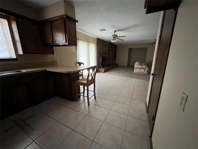3014 S Mission St, Anadarko, OK 73005 - kitchen with ceiling fan, light countertops, light tile patterned flooring, a brick fireplace, and a kitchen breakfast bar