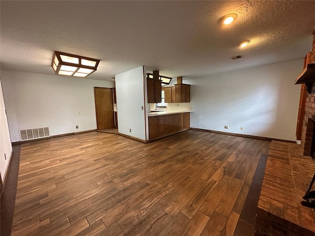 2308 Lynn Ln, Weatherford, OK 73096 - unfurnished living room featuring dark wood finished floors, a brick fireplace, a textured ceiling, and baseboards