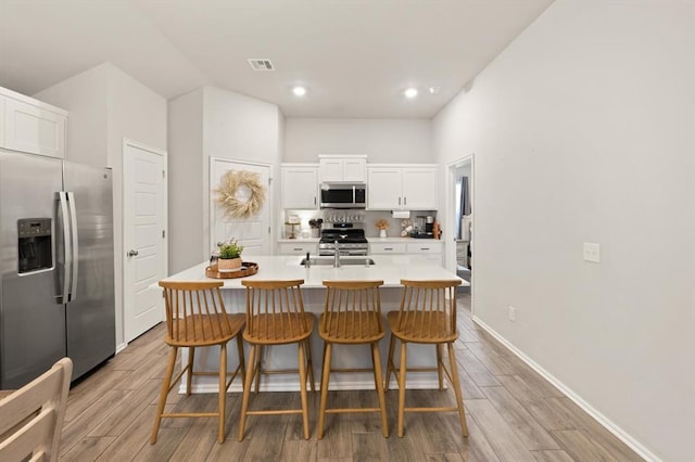 19908 Taggert Dr, Edmond, OK 73012 - kitchen featuring appliances with stainless steel finishes, white cabinetry, a center island with sink, light wood finished floors, and a breakfast bar